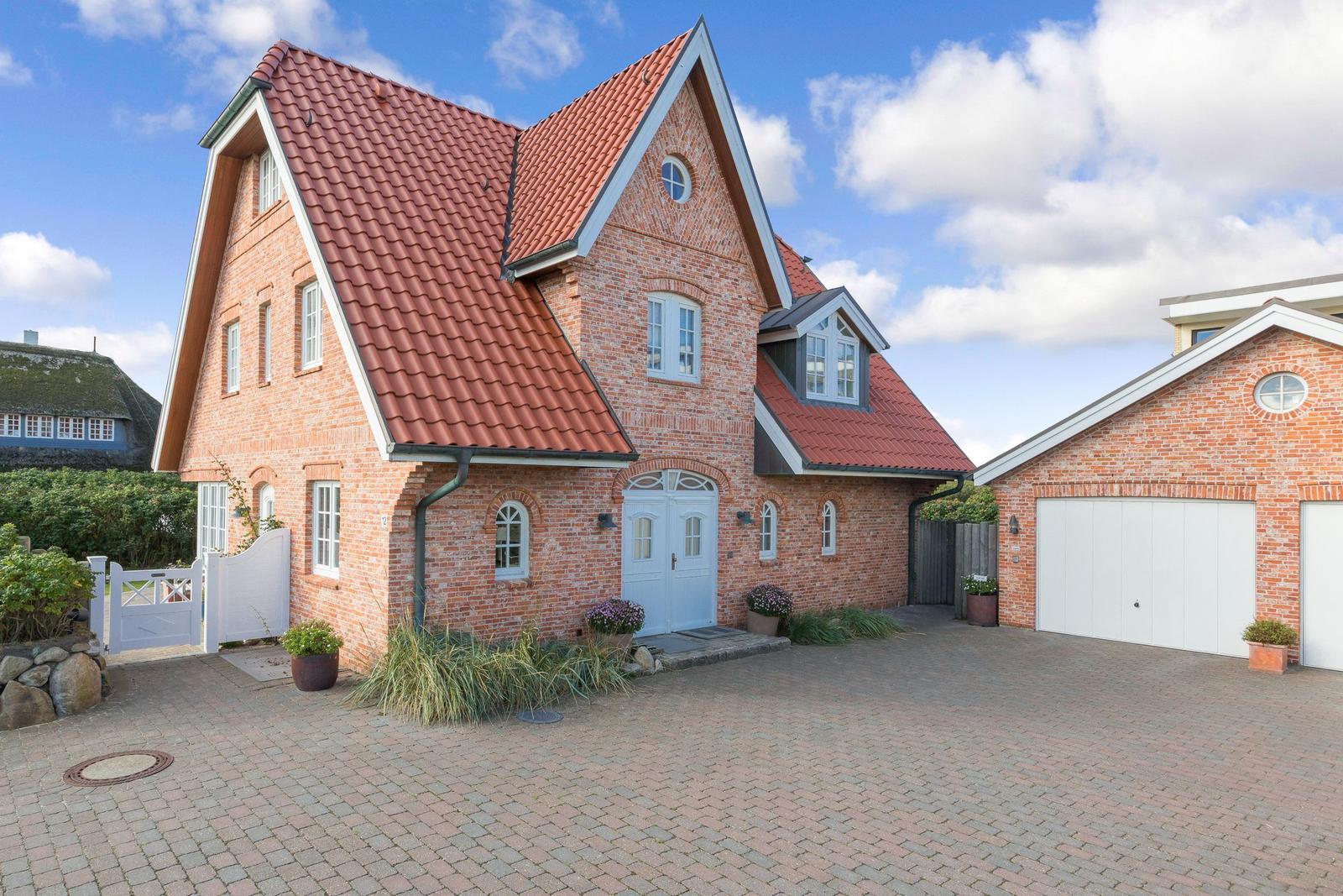 Red tiled roof, brick house with white door and paved courtyard.
