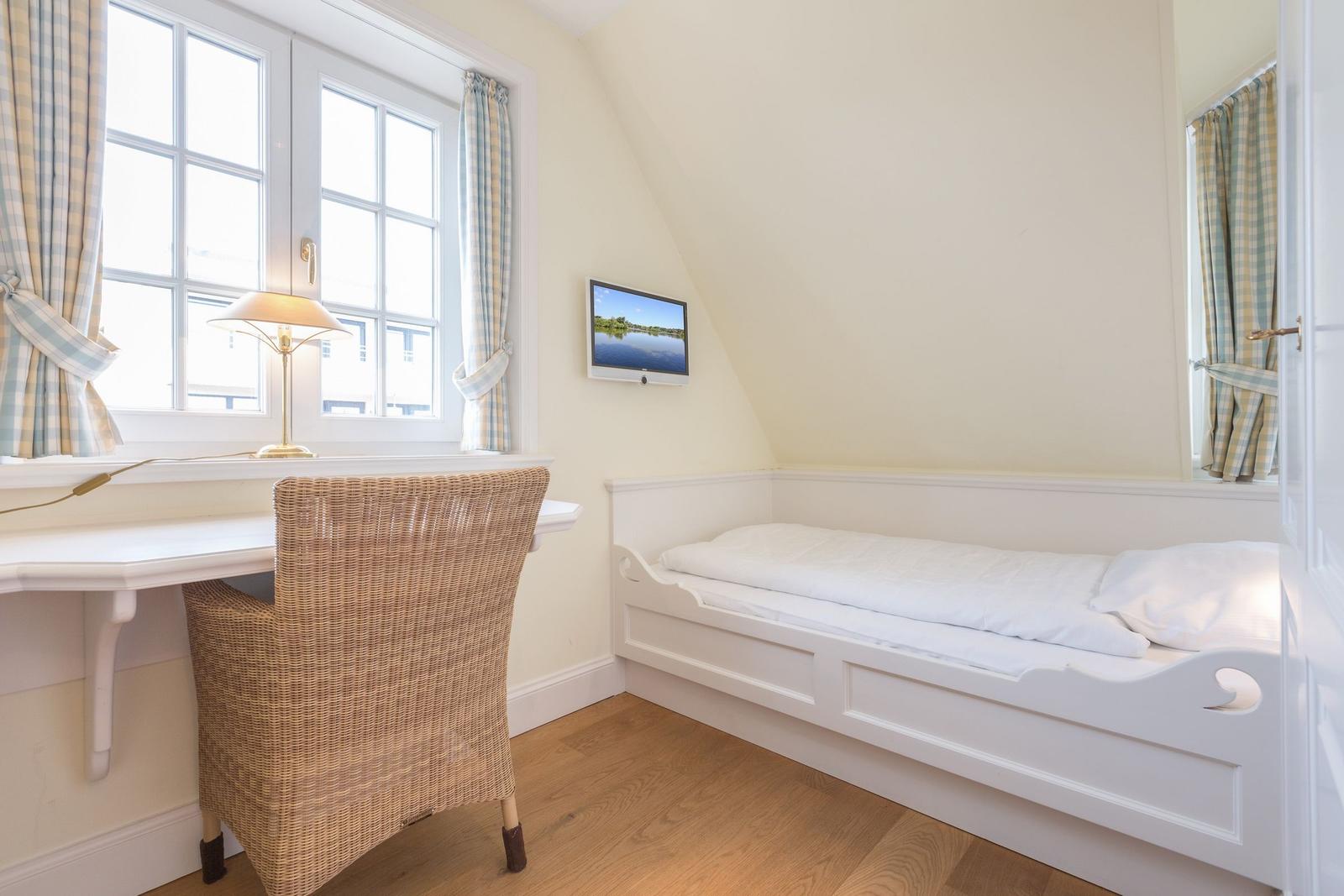 A bedroom with a white bed, desk, and TV on the wall.