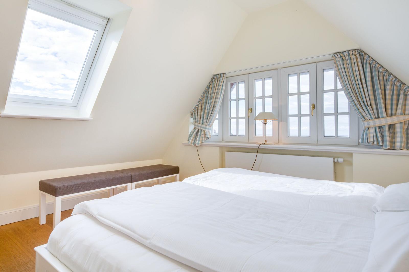 Bedroom with sloped ceiling, large window, and white bed.