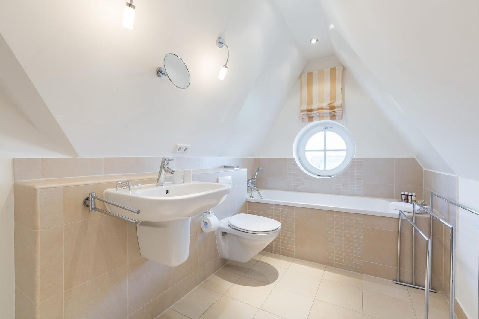 Bathroom with shower, sink, and toilet under sloped ceilings.