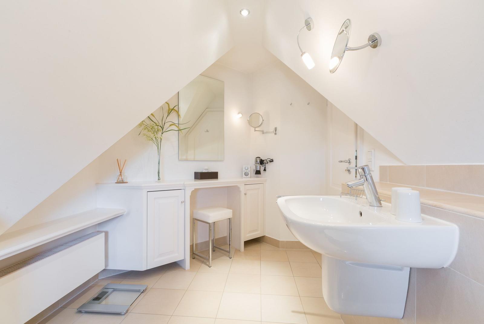 Bathroom with sink, mirror, and makeup station under sloped ceilings.