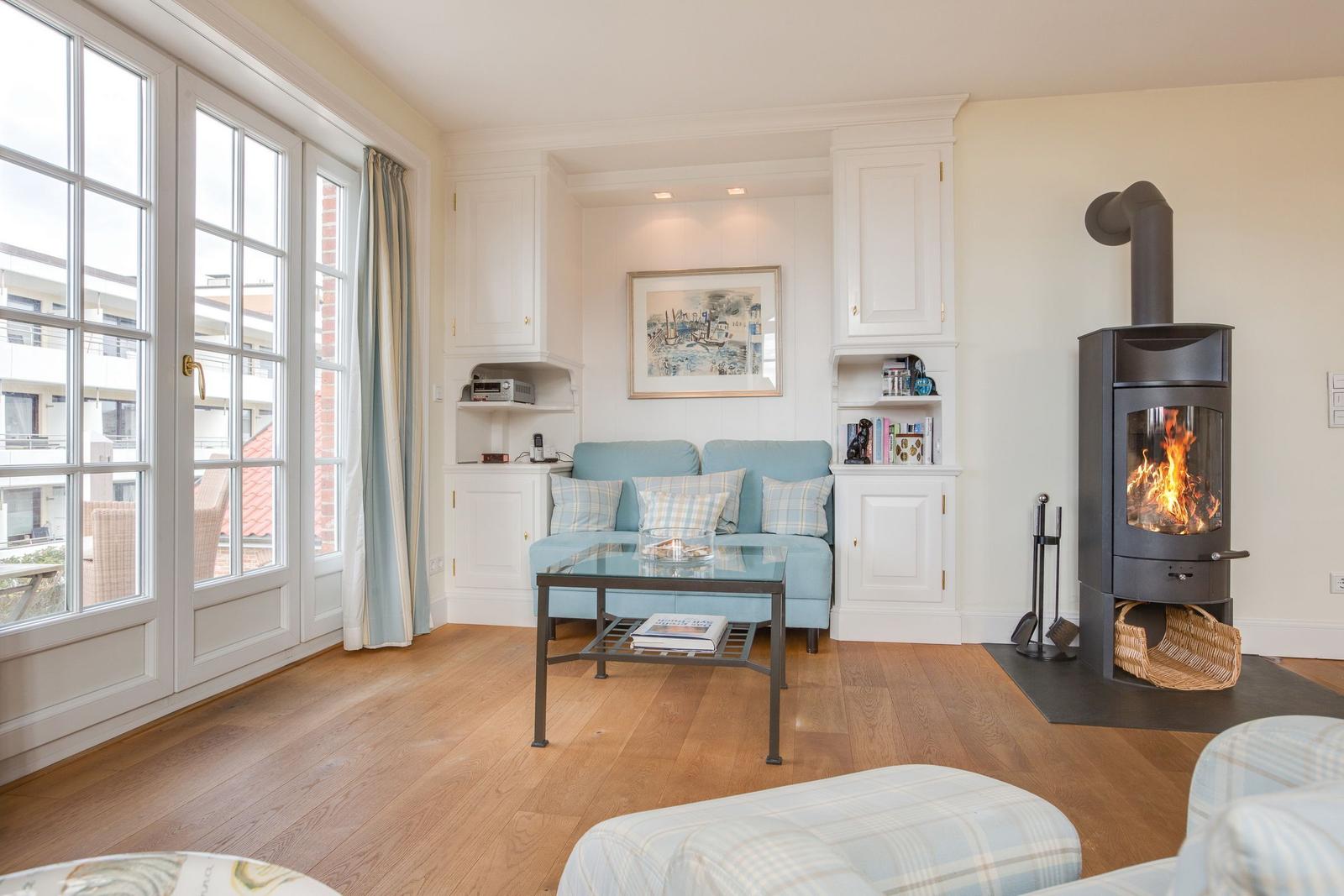 Living room with wooden floor, blue sofa, fireplace and large windows.