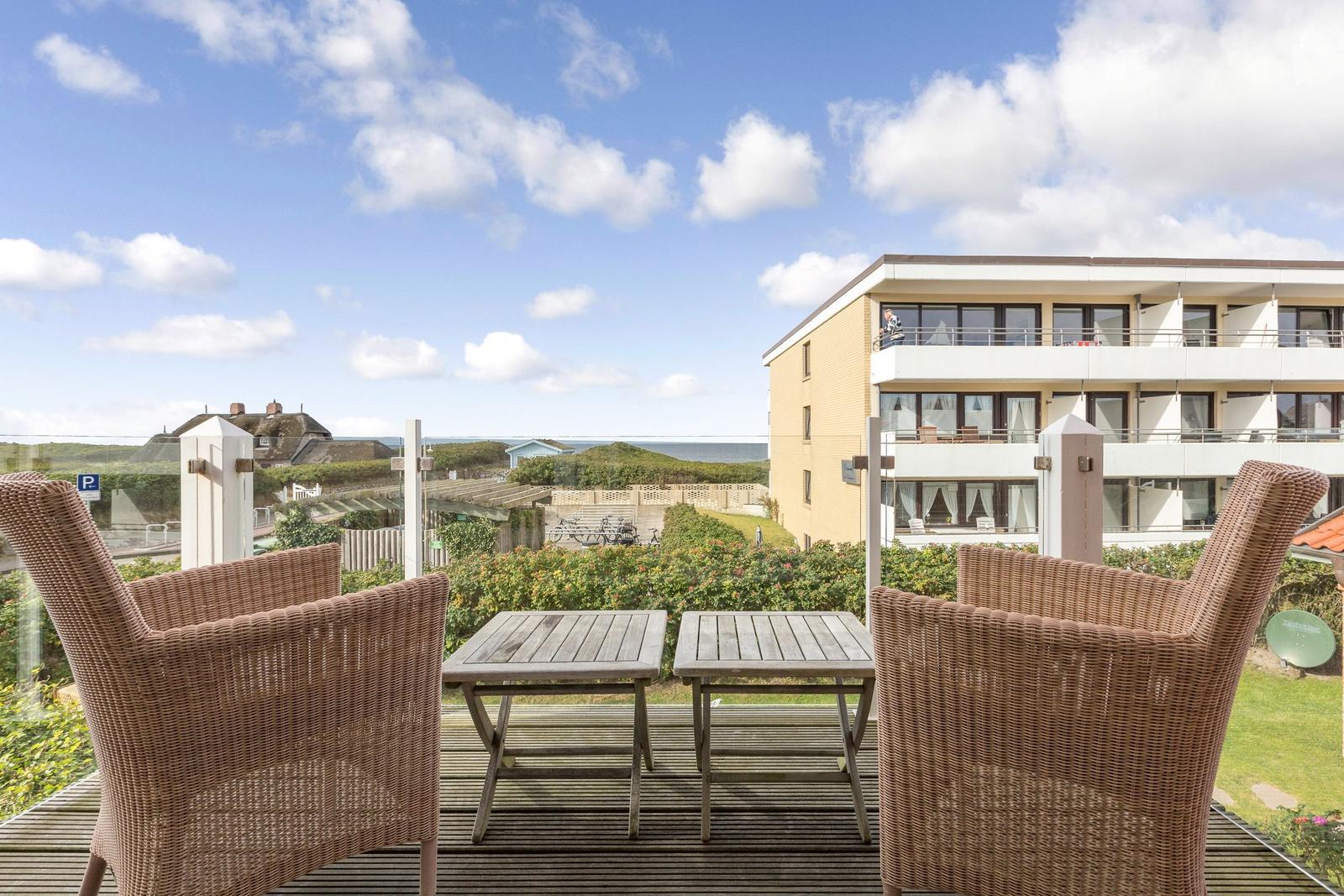 Terrace with two chairs and tables. View of buildings and beach.