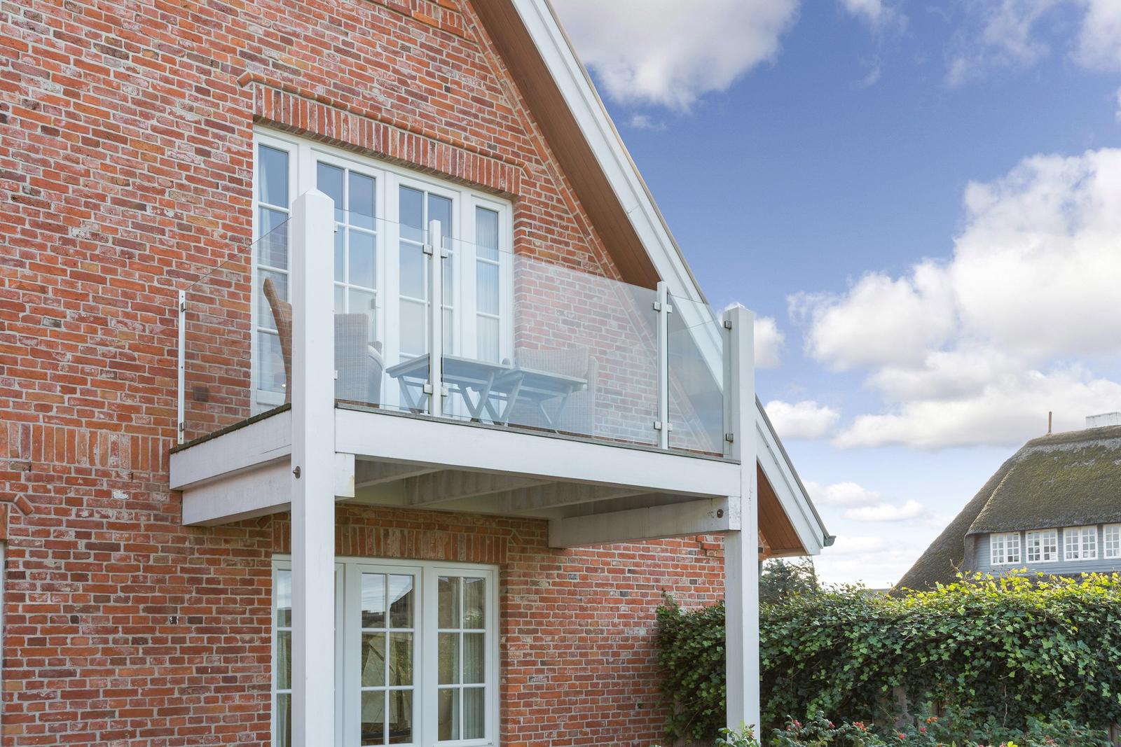 Red brick house with balcony and glass railing under blue sky.