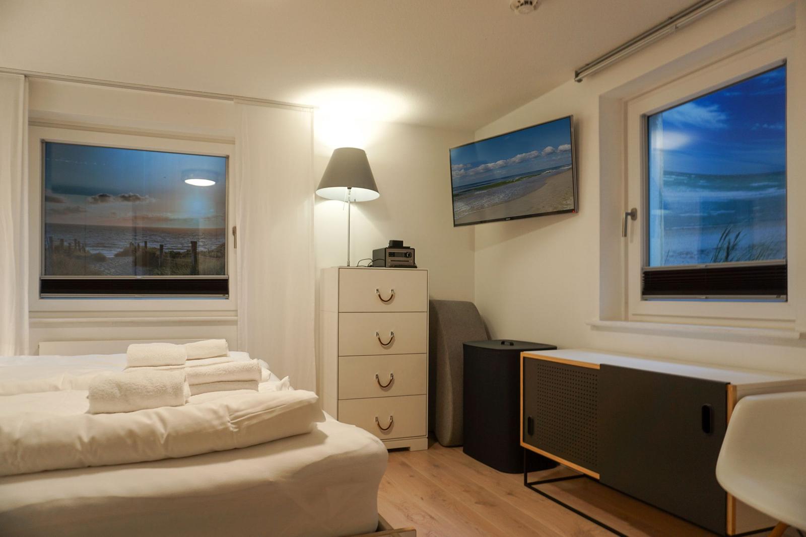 Bedroom with bed, windows, and TV mounted on the wall.