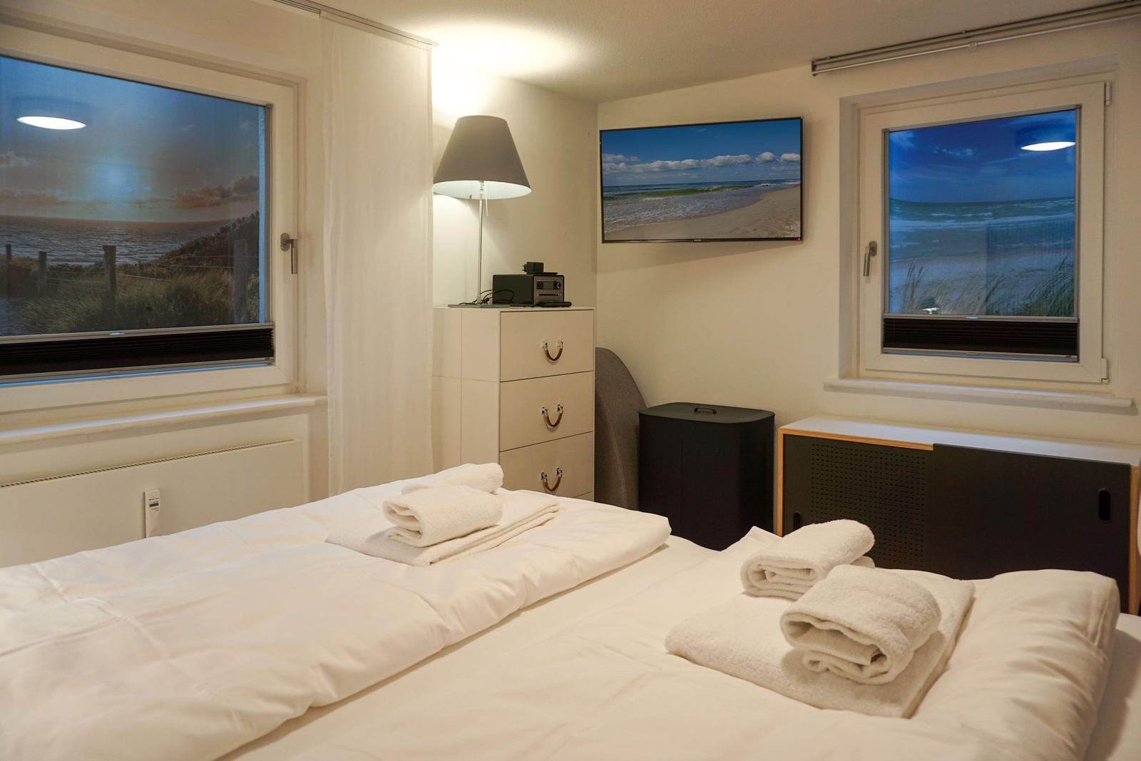 Bedroom with sea view, bed with towels, TV and windows.