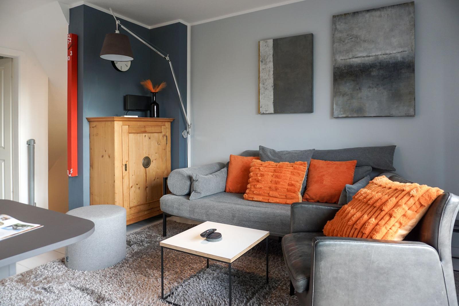 A living room with a gray sofa, orange cushions, and modern wall decor.