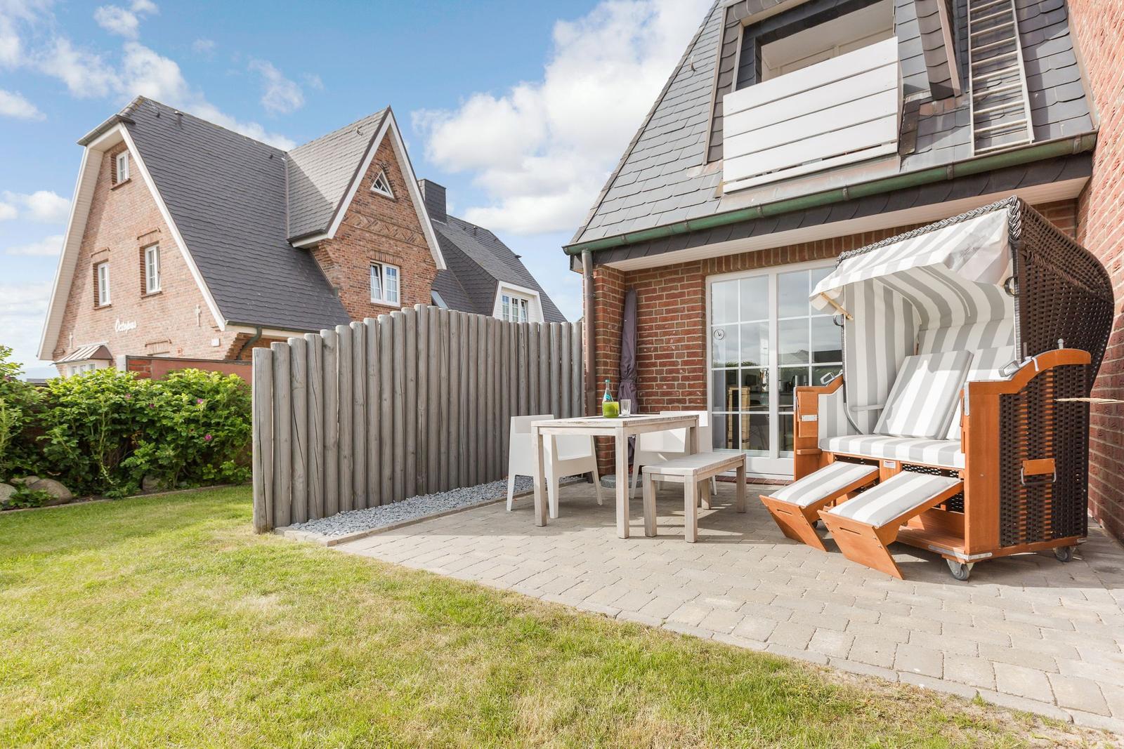 Terrace with lounge chair, table and chairs next to a house with sliding door.