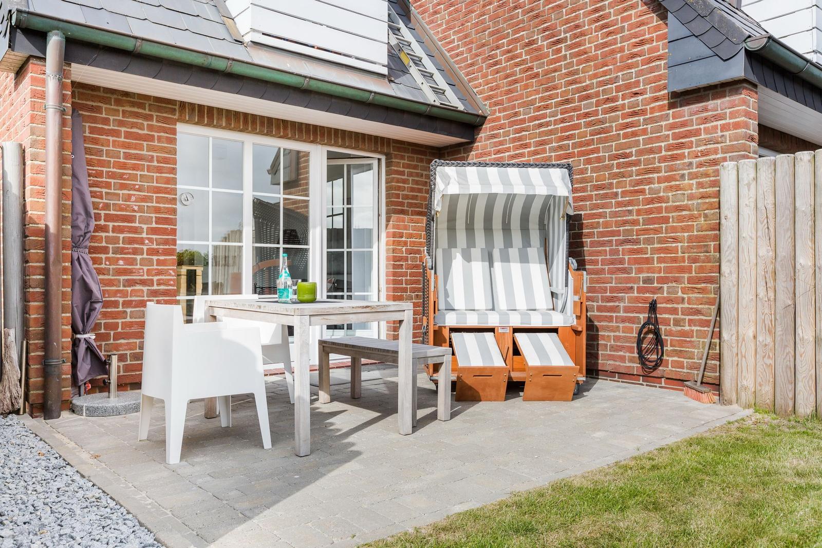 Terrace with table, chairs, and beach chair in front of brick house.