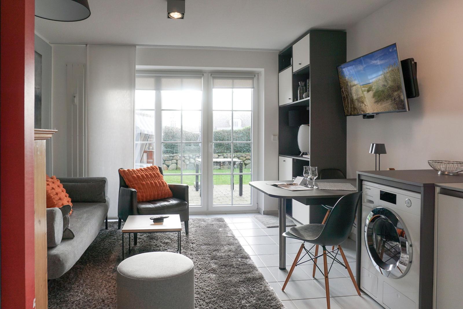 Living area with sofa, armchair, and TV. Doorway to garden. Washing machine in room.