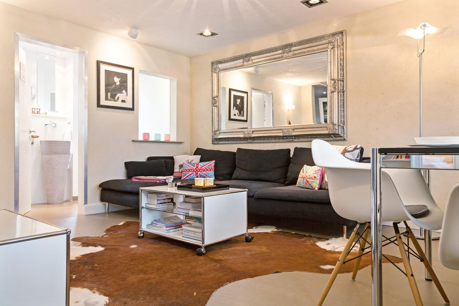 Wohnzimmer mit Sofa, Spiegel und Esstisch. Durchgang zur Badewanne.