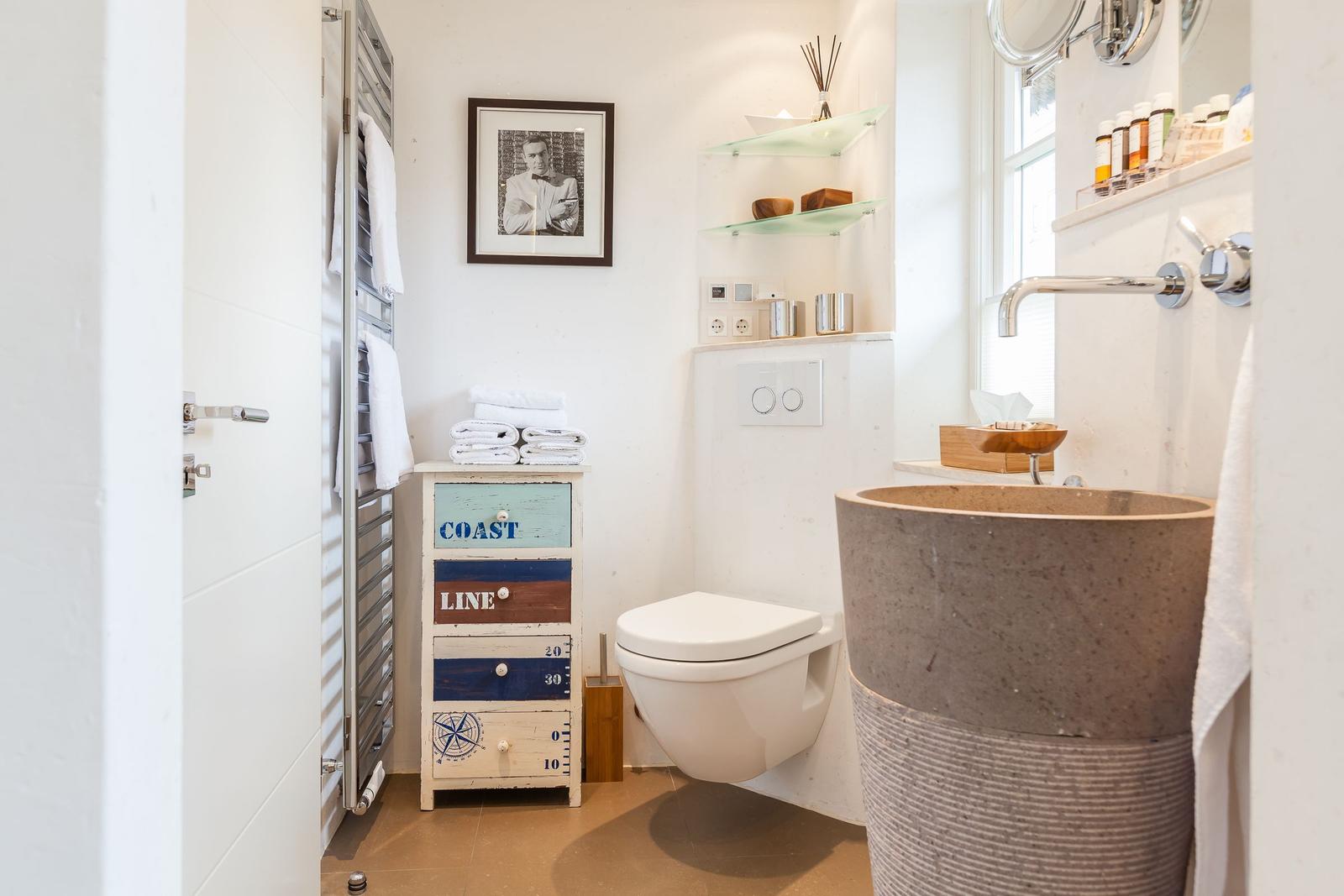 Badezimmer mit Steinwaschbecken, Toilette und Holzschrank mit Aufschrift.