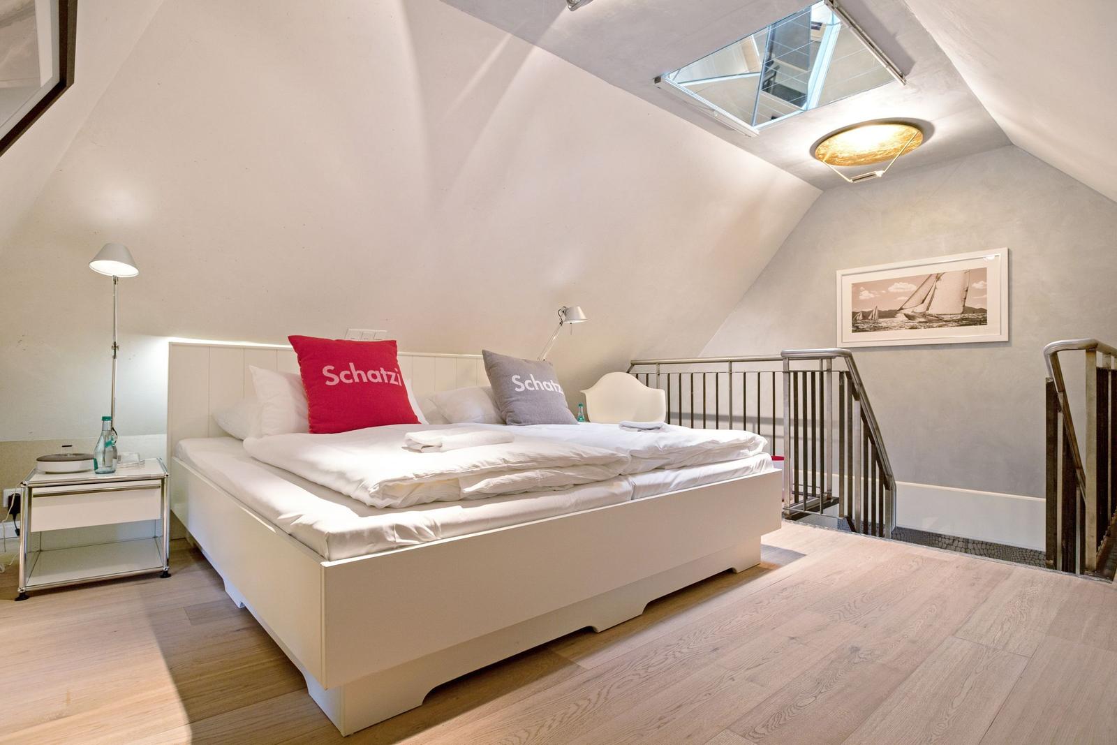 Schlafzimmer mit Dachschrägen, Bett, Nachttisch und Fenster