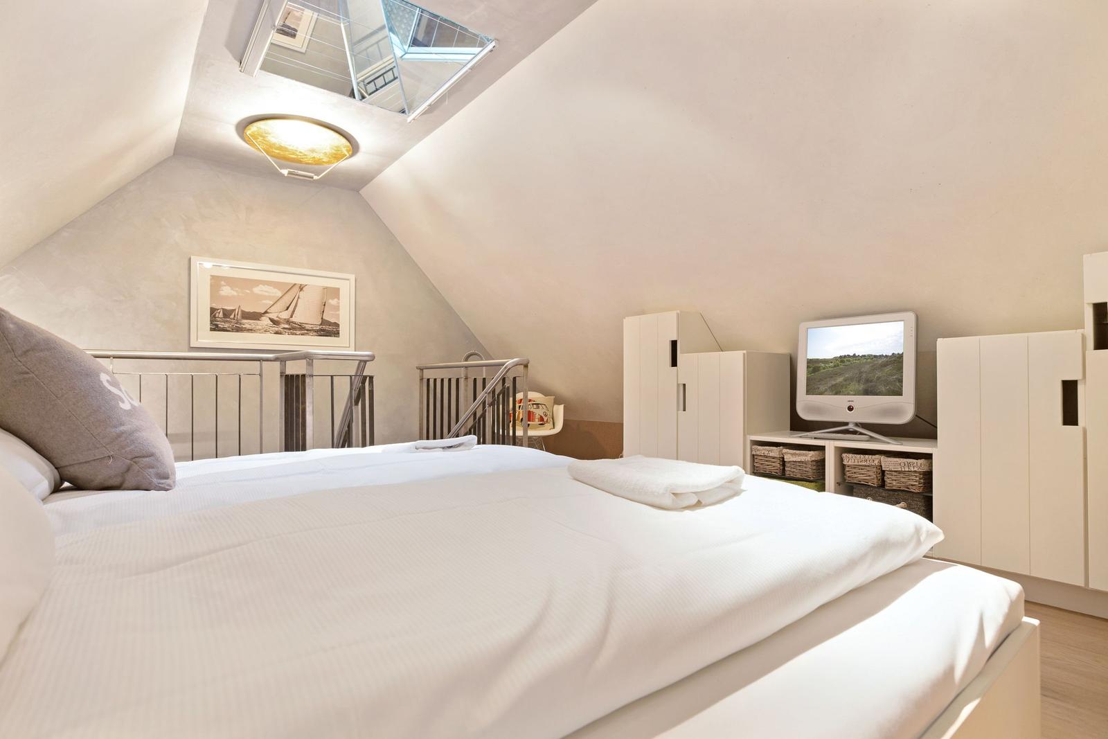 Schlafzimmer mit Dachschrägen, Bett, TV und Kleiderschrank.