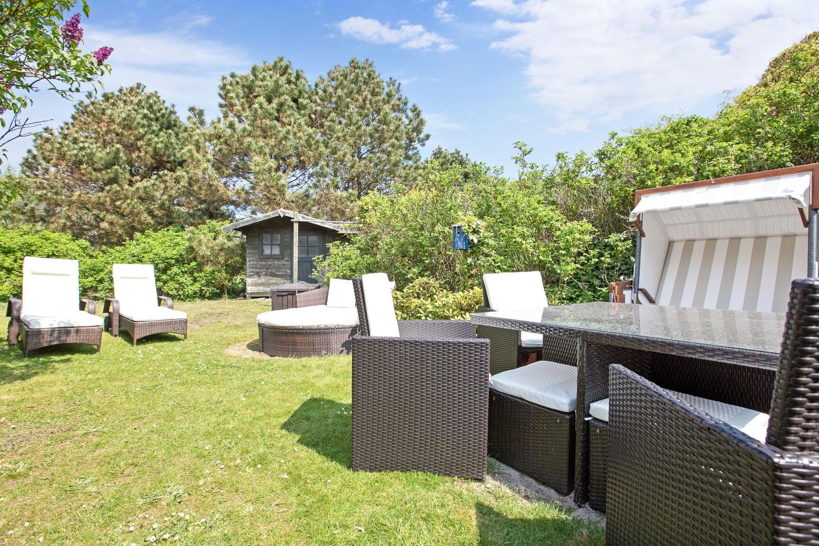 Garten mit Sitzgruppe, Sonnenschutz und Grillplatz. Hintergrund: Wald und kleine Hütte.