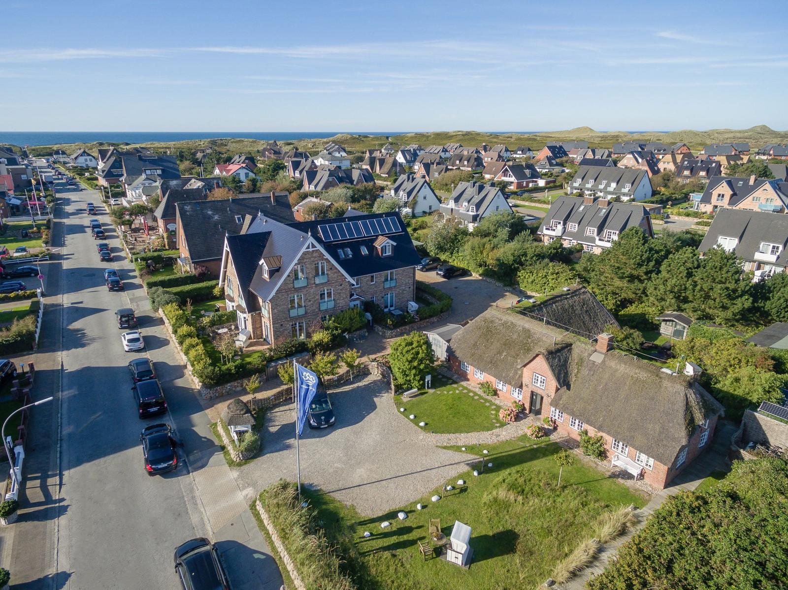 Haus mit Dachgauben und Solaranlage, umgeben von Grünflächen und einem Straßenzug mit Autos.
