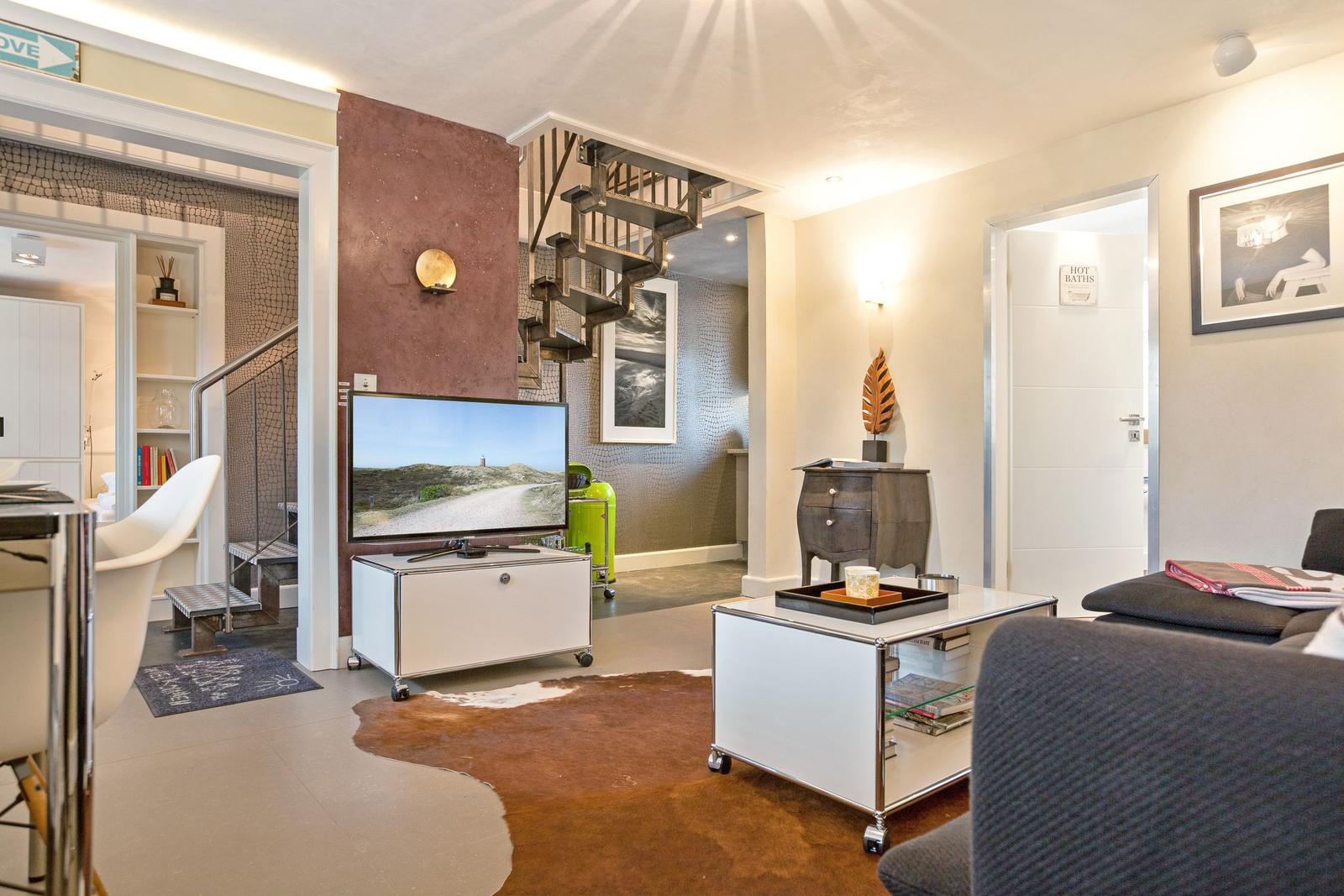 Wohnzimmer mit Fernseher, Couch und Treppenhaus.