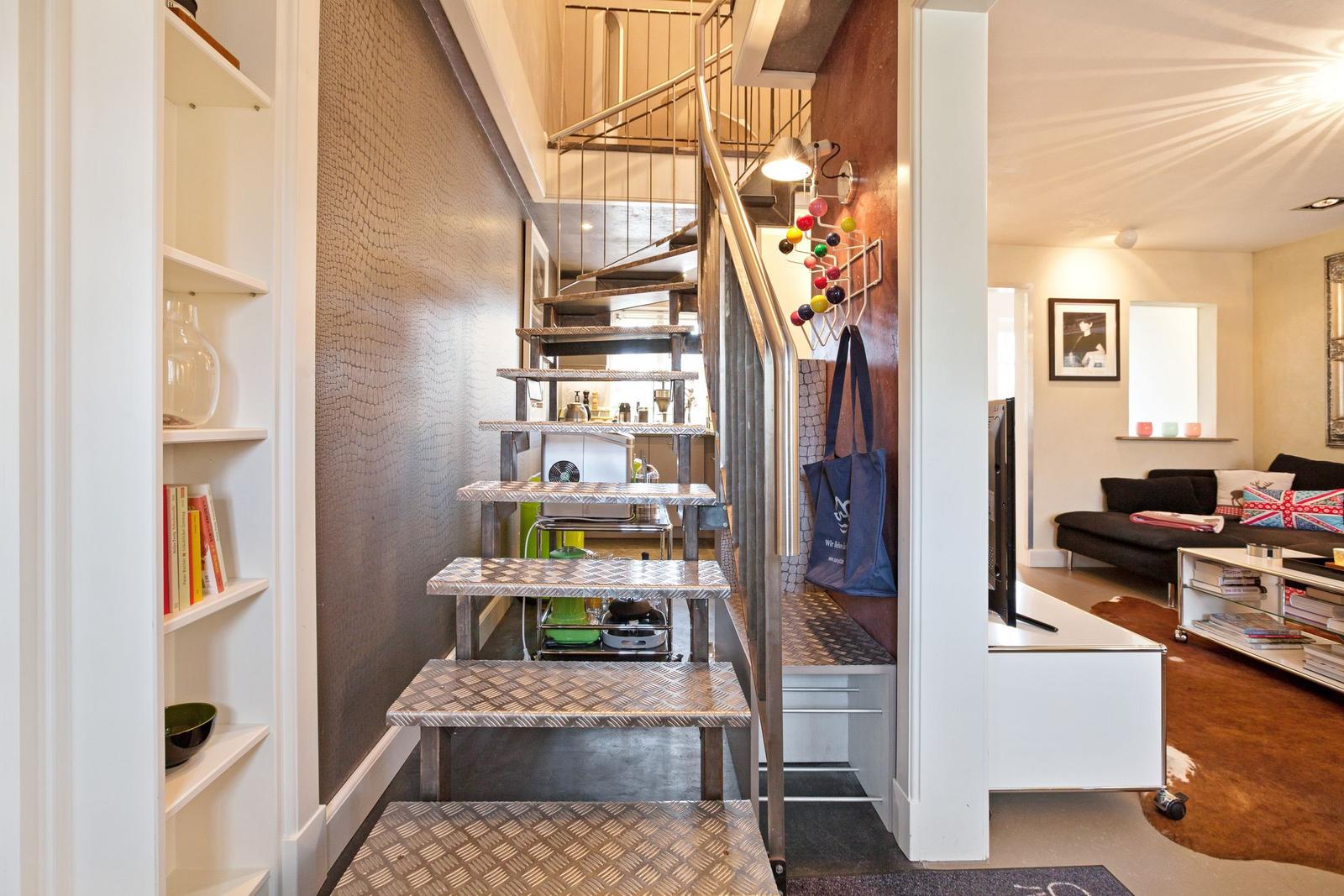 Treppenhaus mit Metalltreppe und Bücherregal. Wohnbereich mit Sofa und Fernseher.