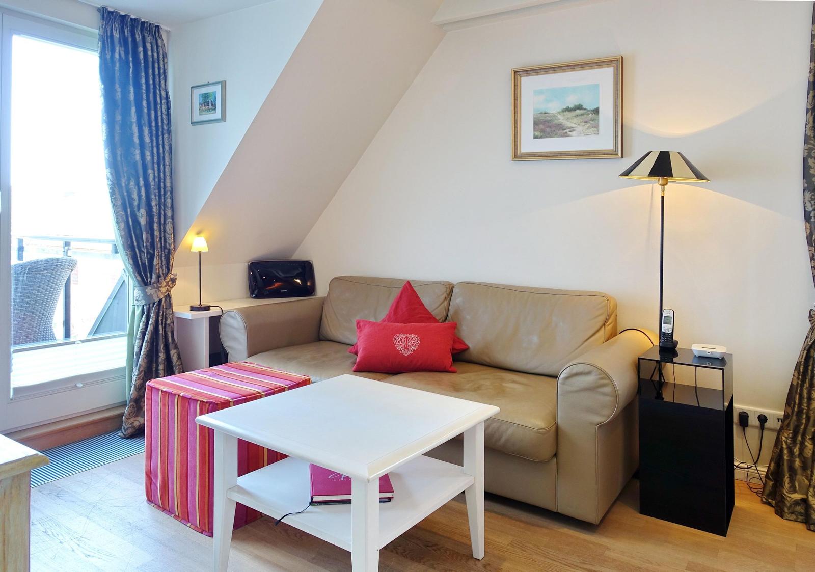 Living room with sofa, table, and window. Sloped ceiling and curtains visible.