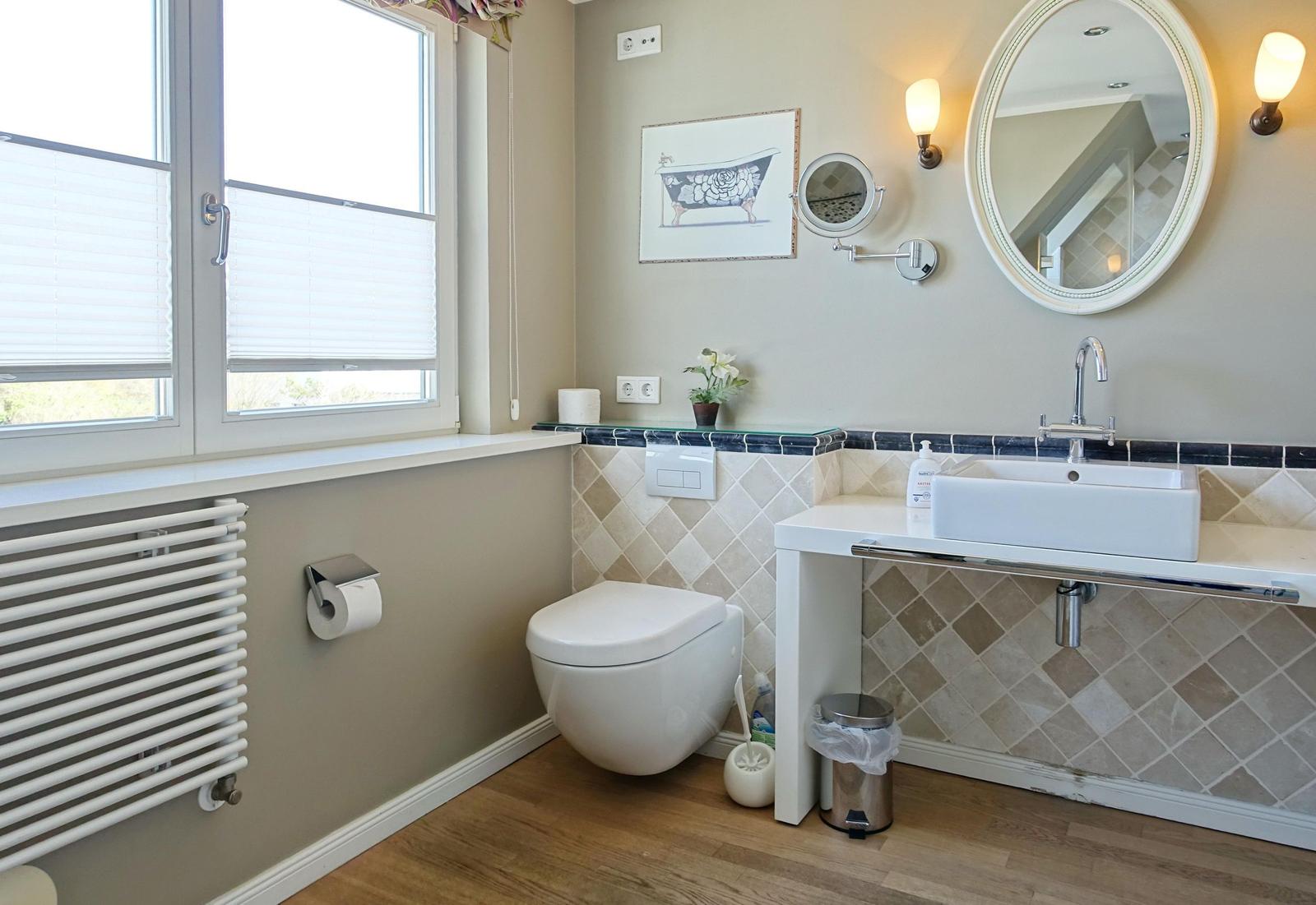 Bathroom with toilet, sink, and window. Tiled wall and wooden floor.