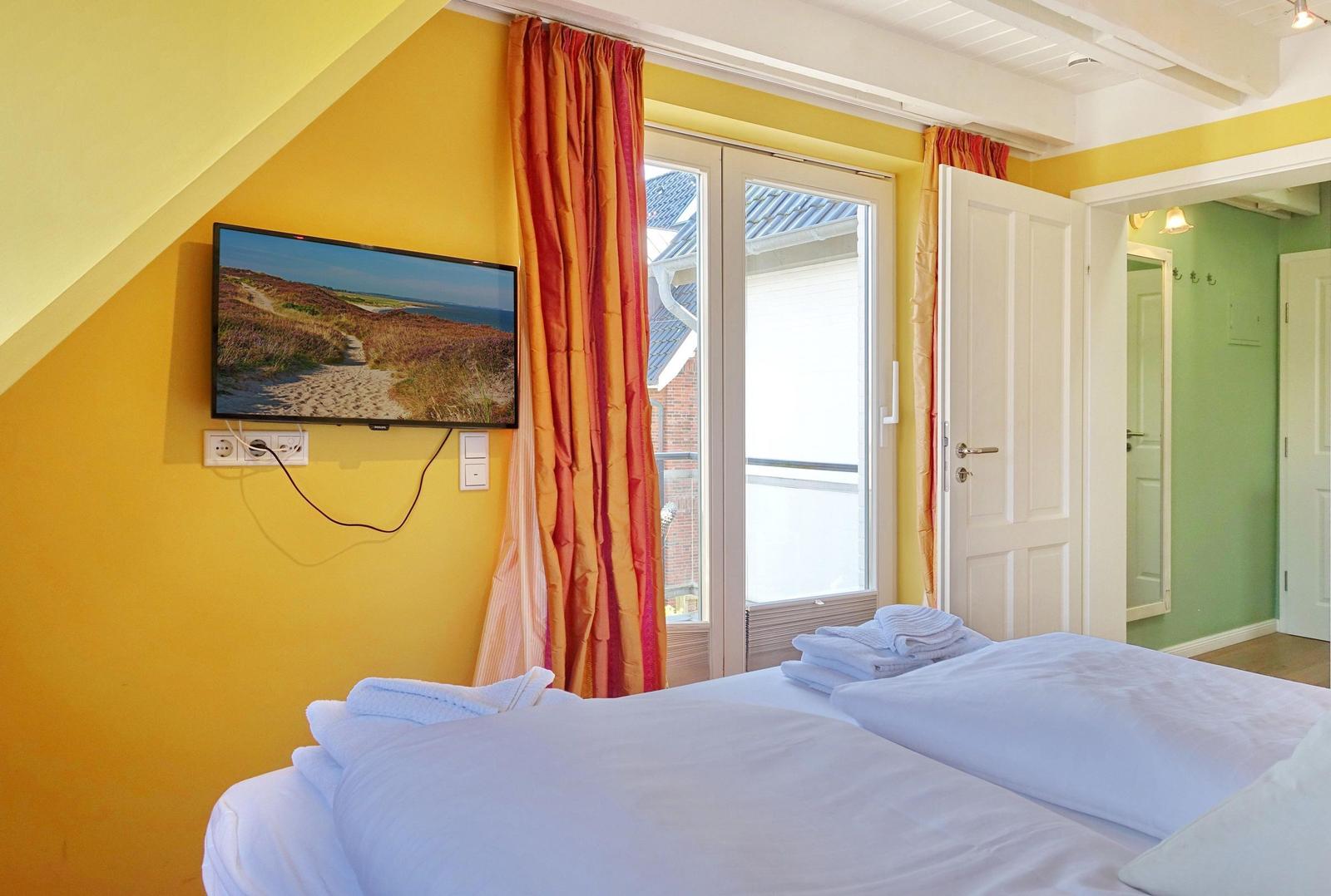 Bedroom with bed, TV, and window. Yellow walls and orange curtains.