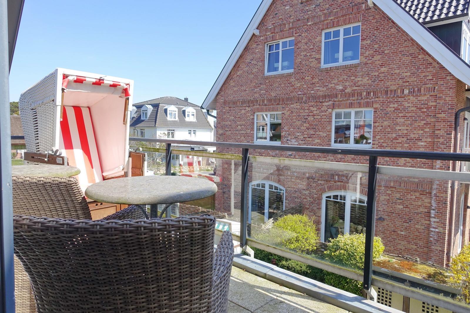 Terrace with lounge chair and table, view of brick house and garden.