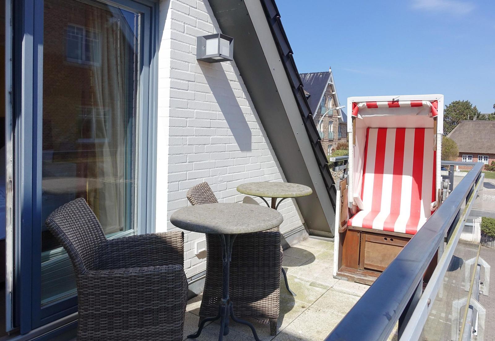 Terrace with two chairs, table, and beach chair. Background: house and clear sky.