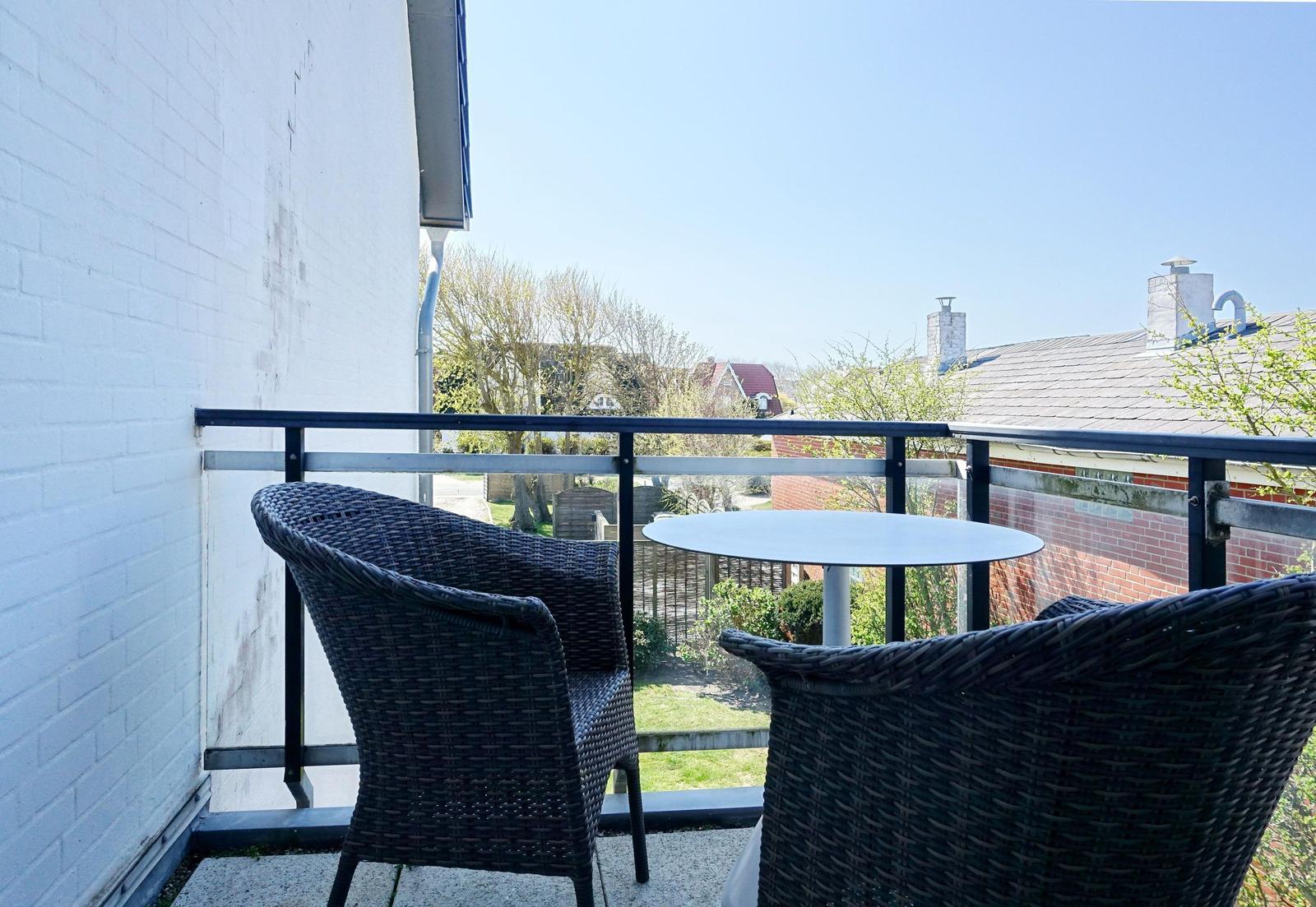 Terrace with table and two chairs, view of garden and rooftops.