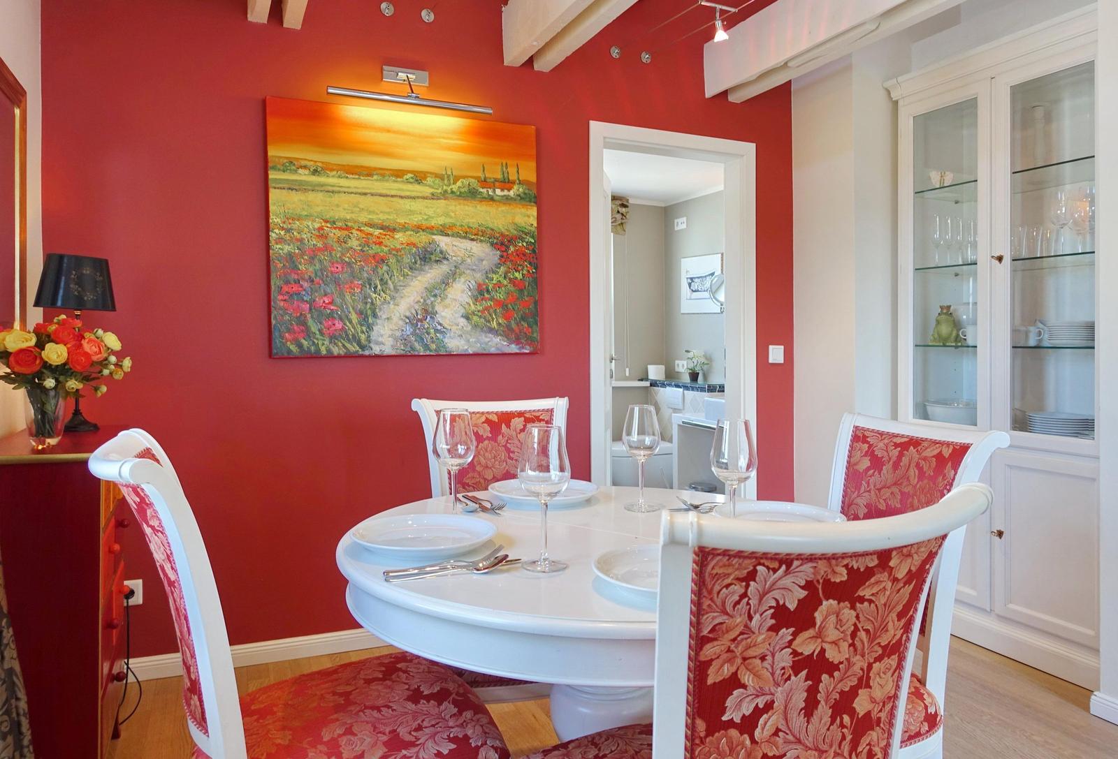 Red dining room with round table, chairs, and wall painting.