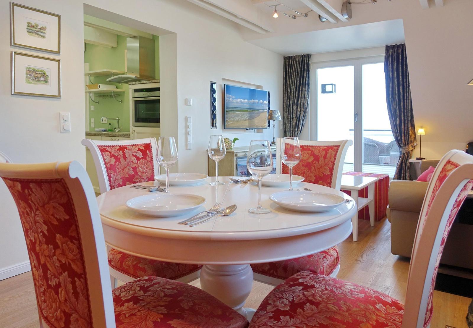 Round table with chairs, TV, and kitchen area in the background.