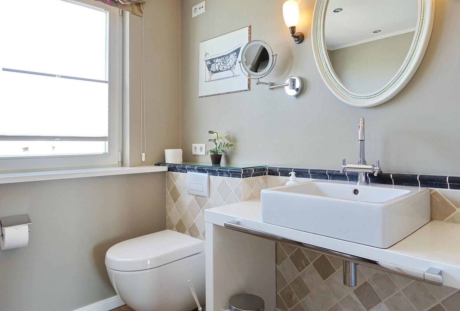 Bathroom with sink, mirror, and toilet. Window, wall art, and plant visible.