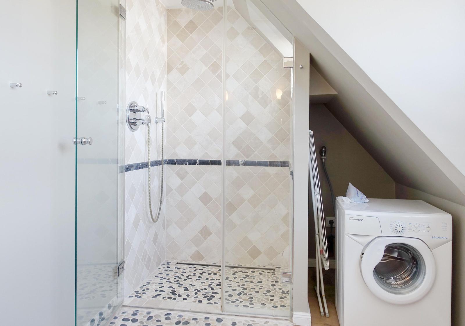 Shower with glass enclosure and washing machine under sloped ceiling