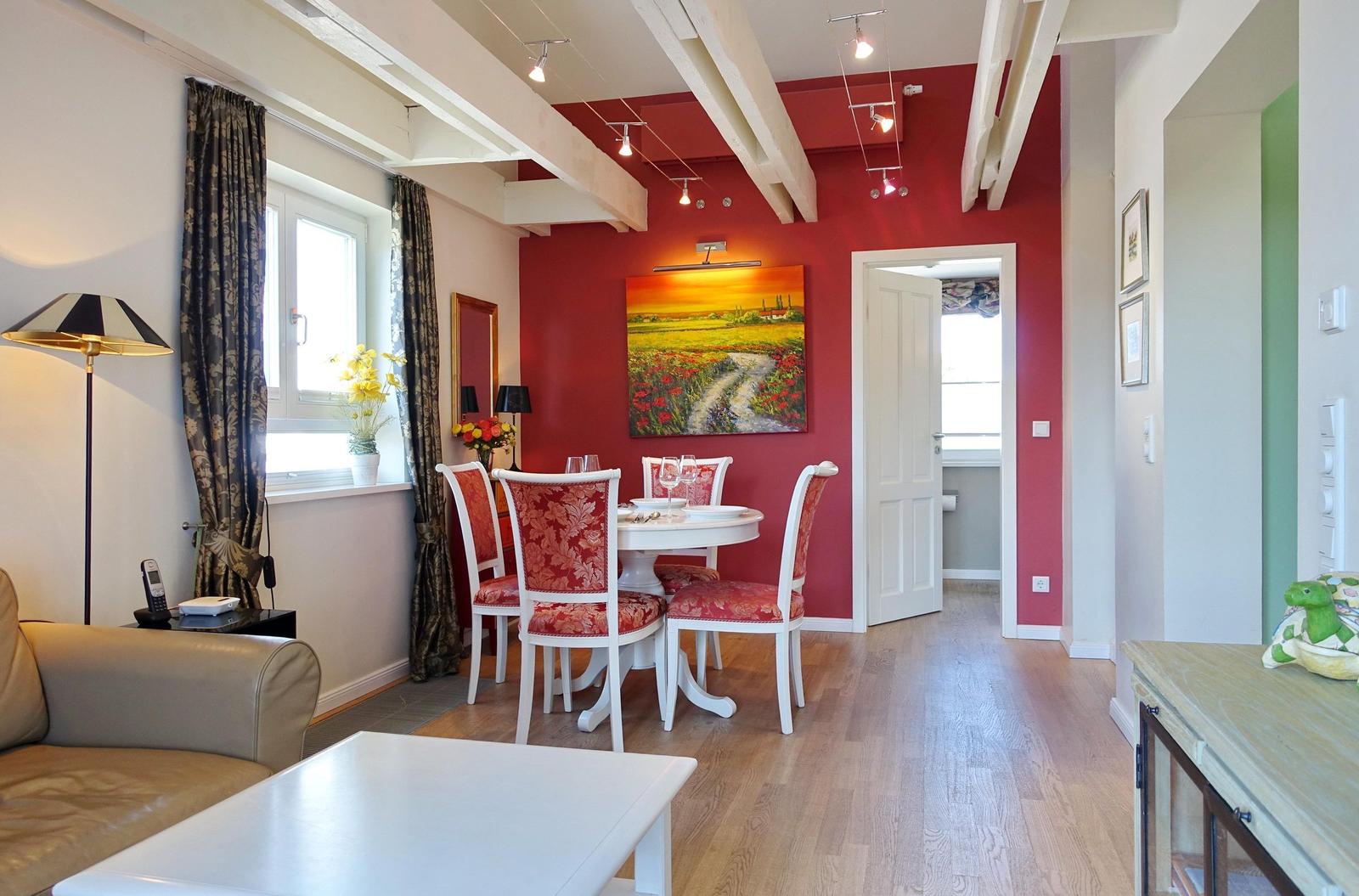 Dining area with table, chairs, and wall art. Wooden floor and ceiling beams.