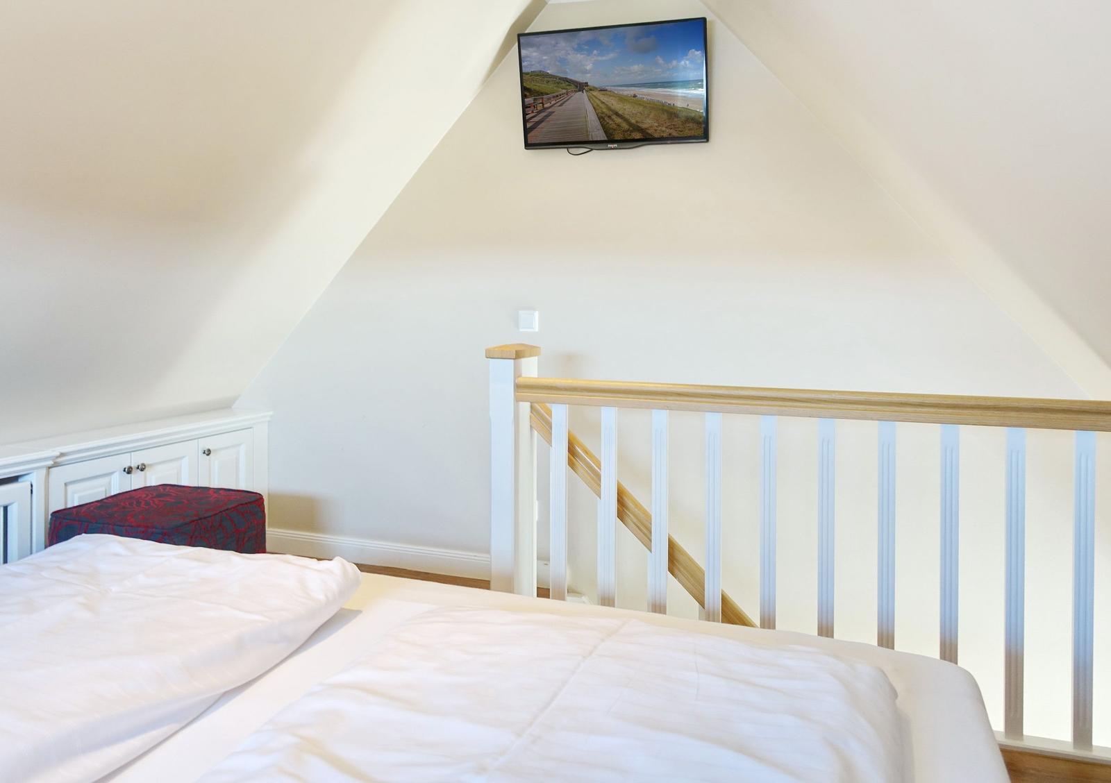 Bedroom with sloped ceiling, bed, and TV mounted on the wall.