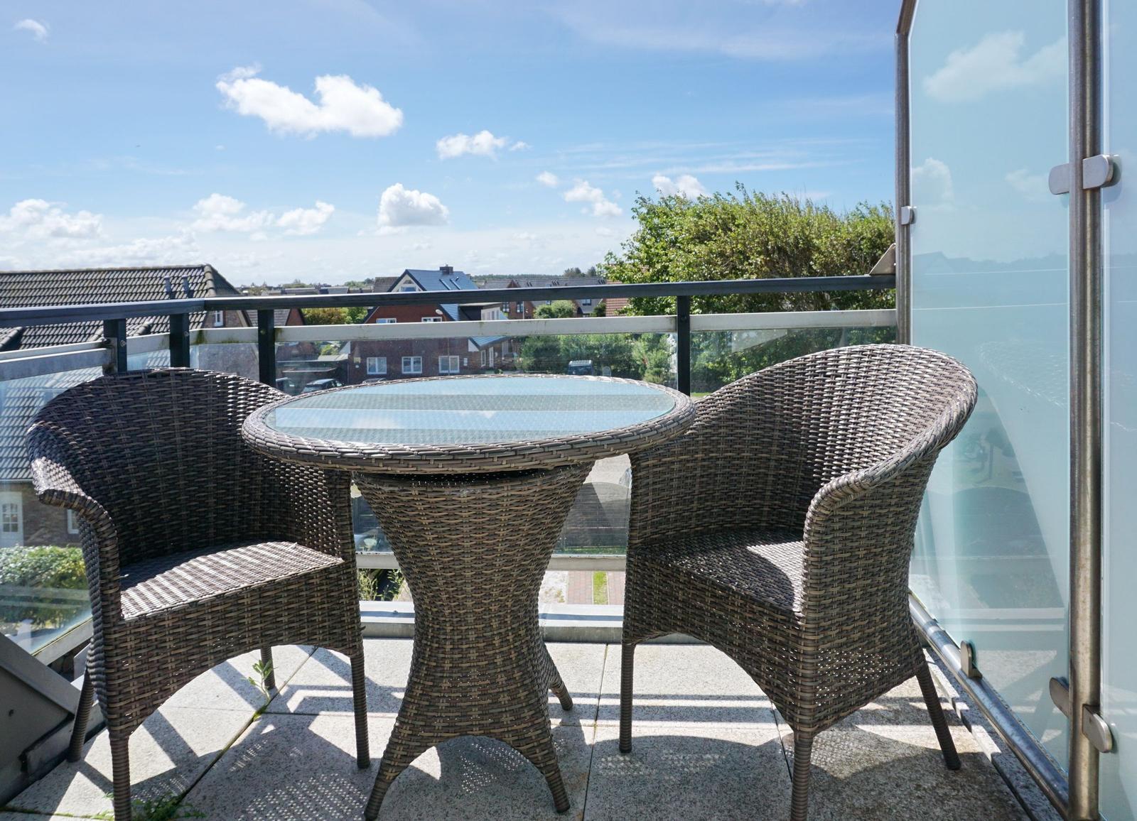 Terrace with table and two chairs. View of residential area and sky.