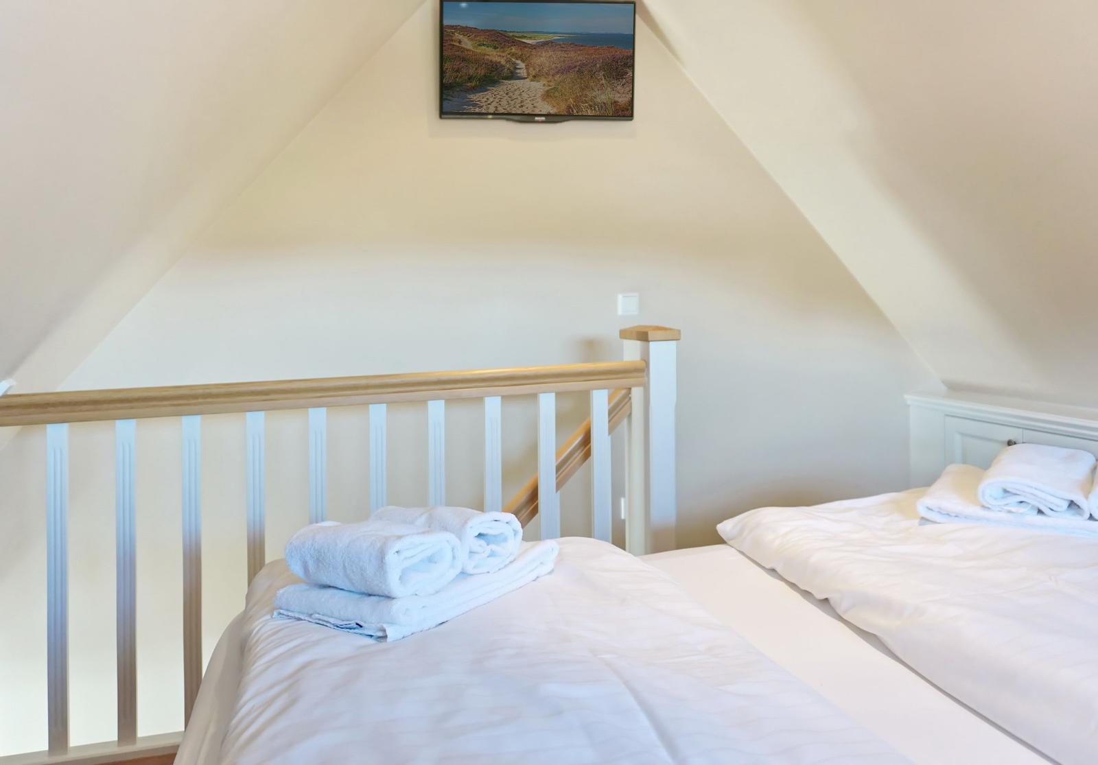 Two beds with white linens and towels under a dormer window.