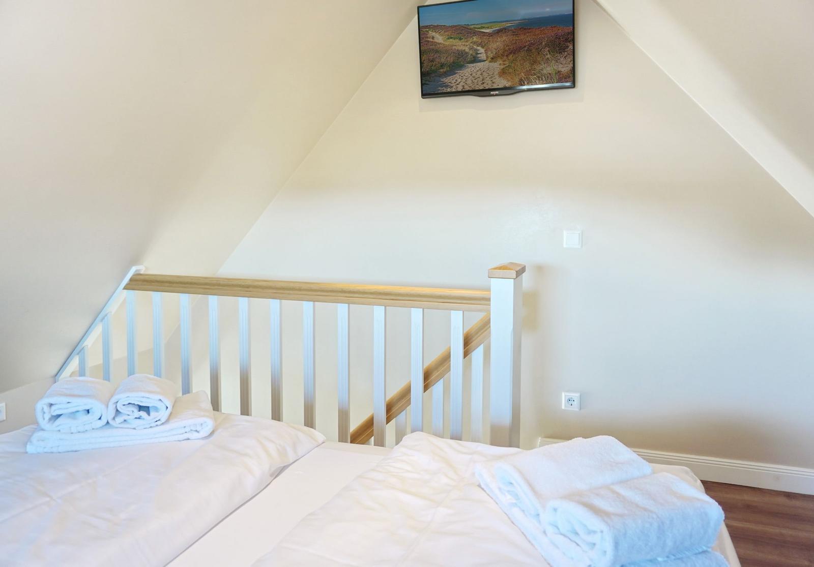 Bedroom with double bed, towels, and TV mounted on the wall.
