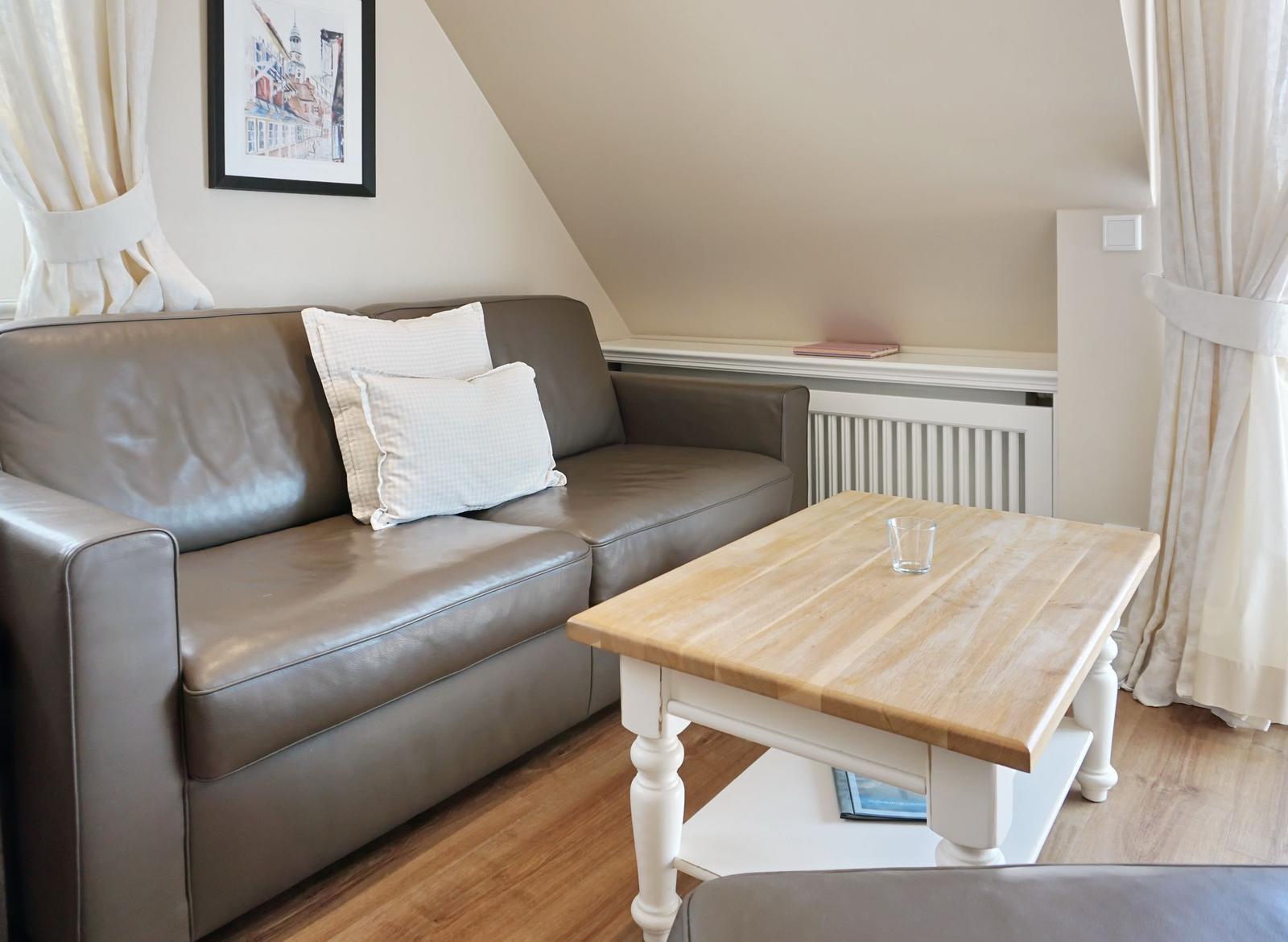 A living room with a gray sofa, a wooden table, and white curtains.