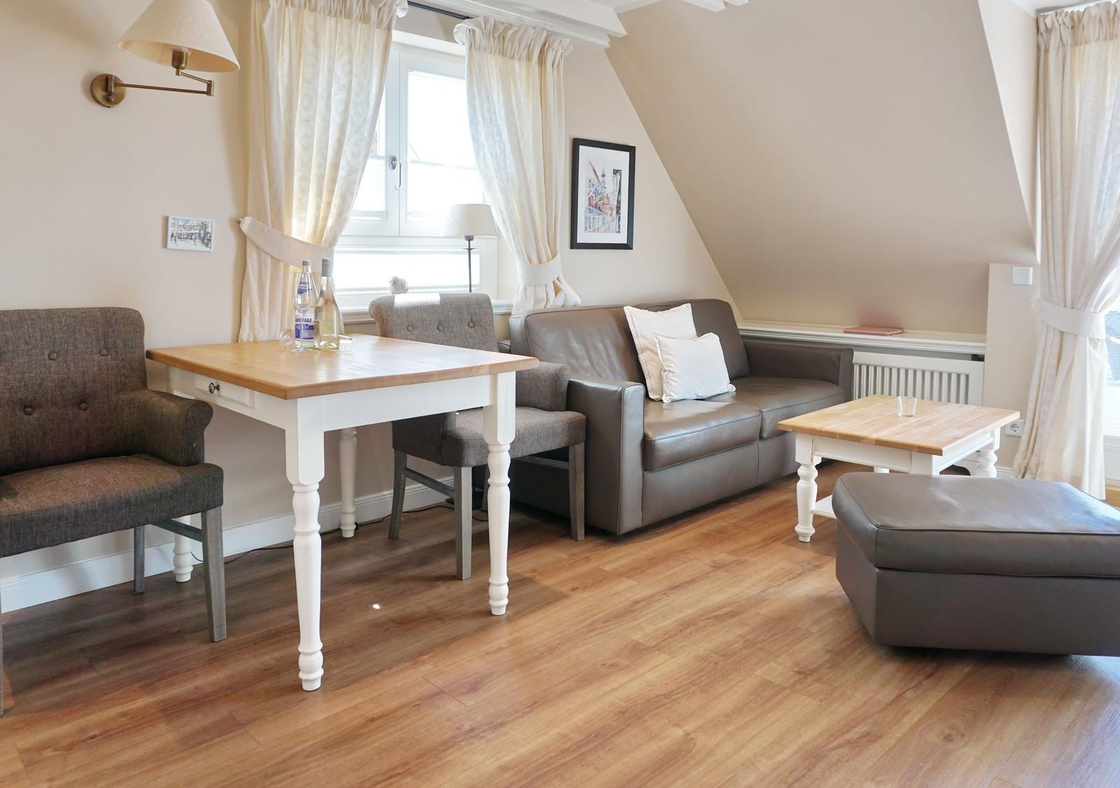 Living room with sofa, table, and window. Wooden floor and cream-colored walls.