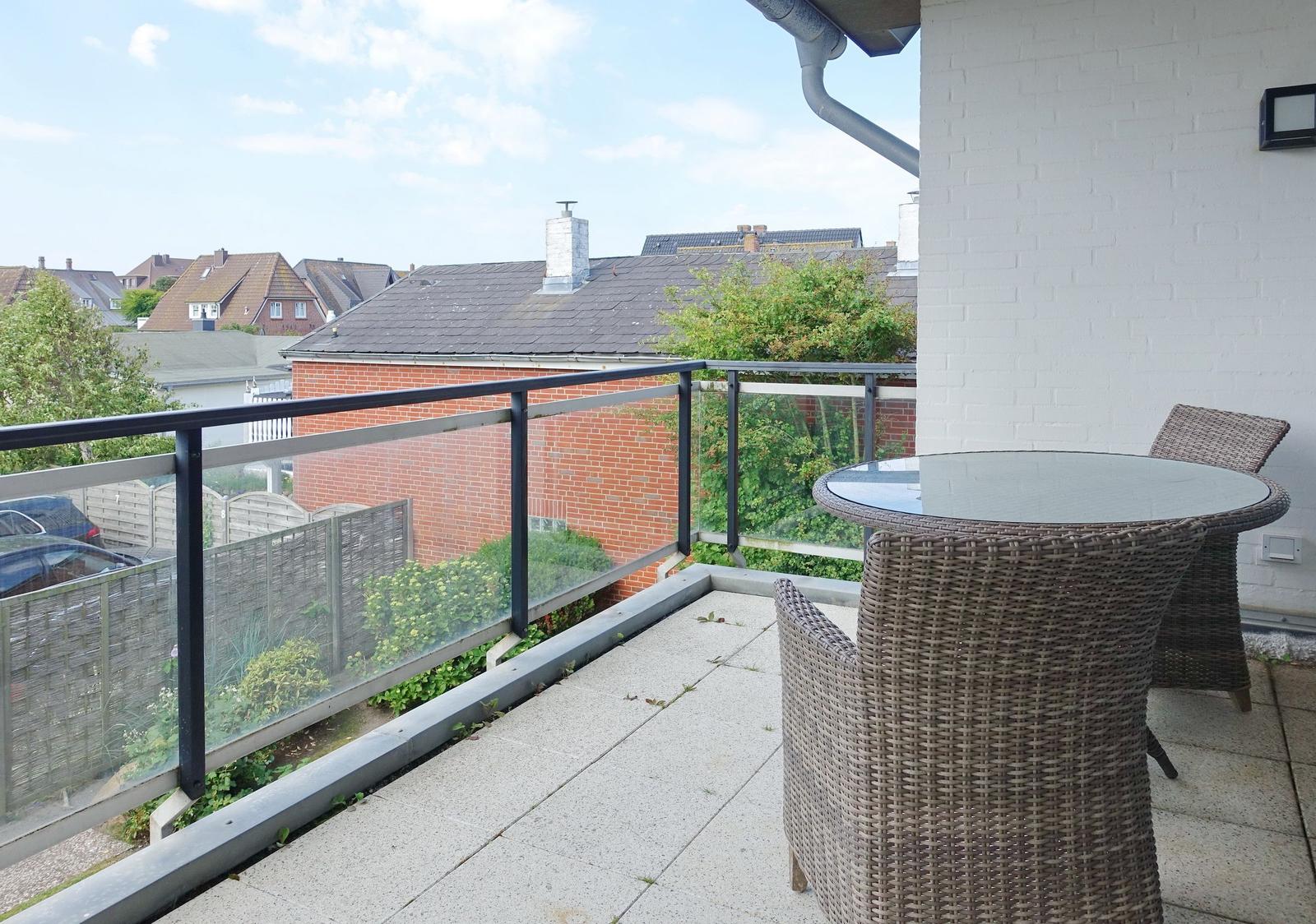Terrasse mit Tisch und Stühlen, Blick auf Wohnhäuser und Grünflächen.
