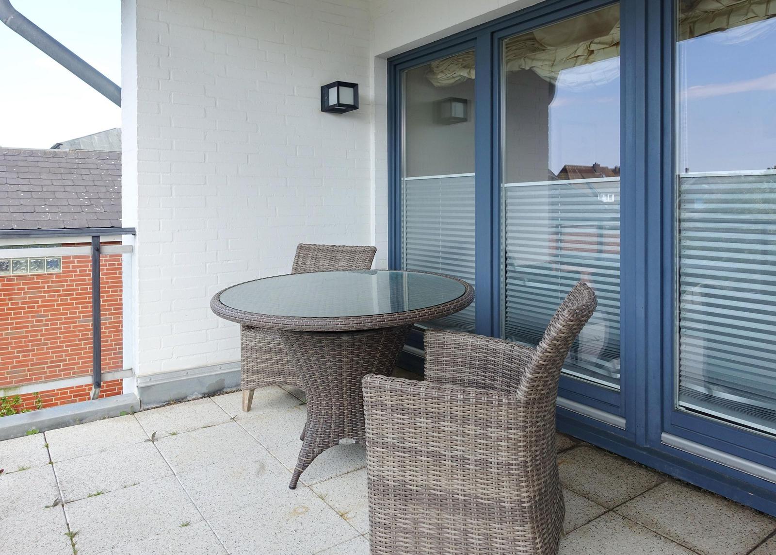 Terrasse mit Rattan-Tisch und Stühlen, Glas-Tür und weißer Wand.
