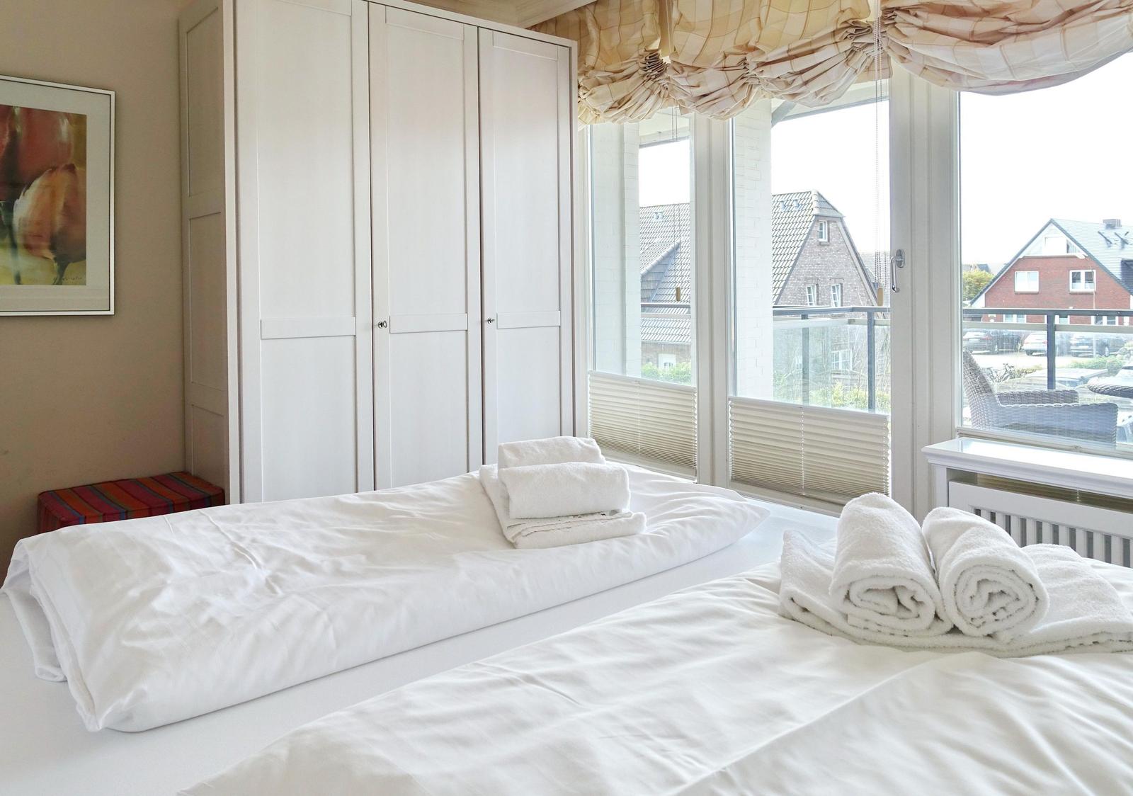 Zwei Betten mit weißen Laken und Handtüchern. Große Fenster mit Blick auf die Straße.
