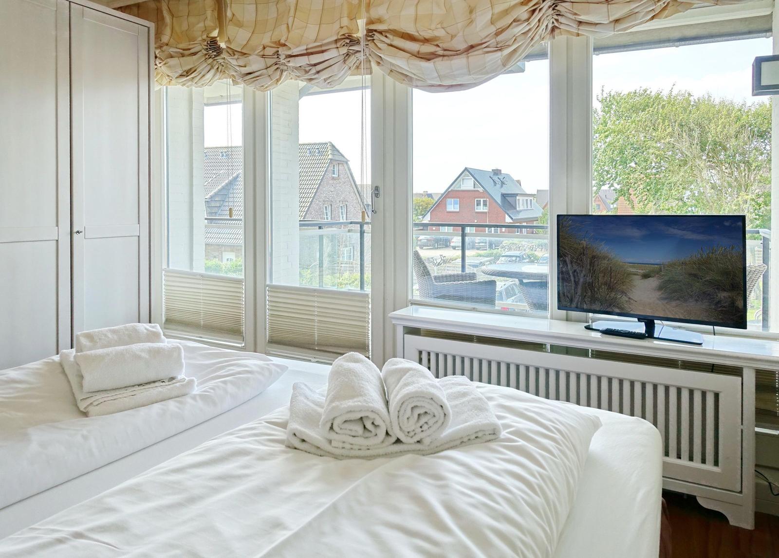 Zimmer mit Bett, TV und Blick auf Balkon mit Sitzgelegenheiten.