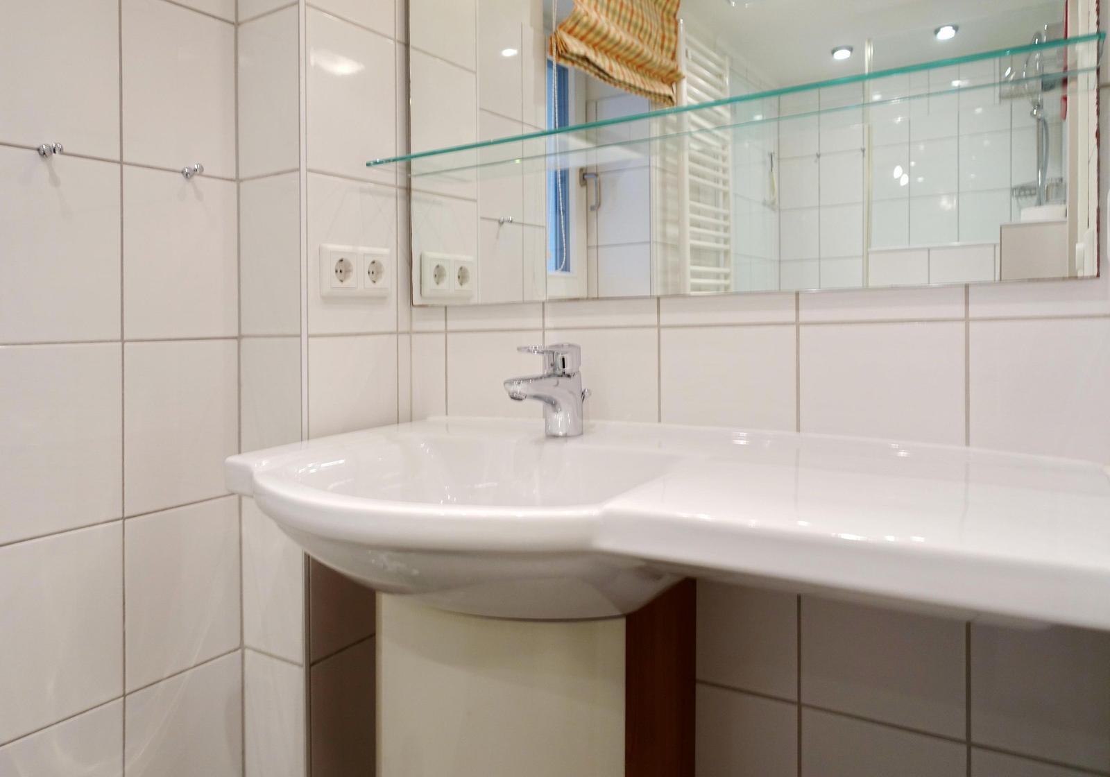 Sink with mirror and glass shelf in white tiled wall