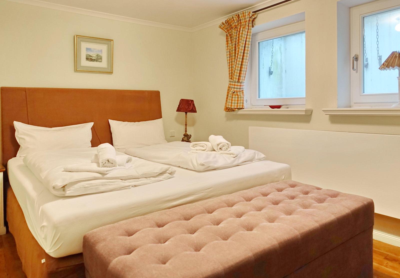 A bedroom with a double bed, windows, and a bench.
