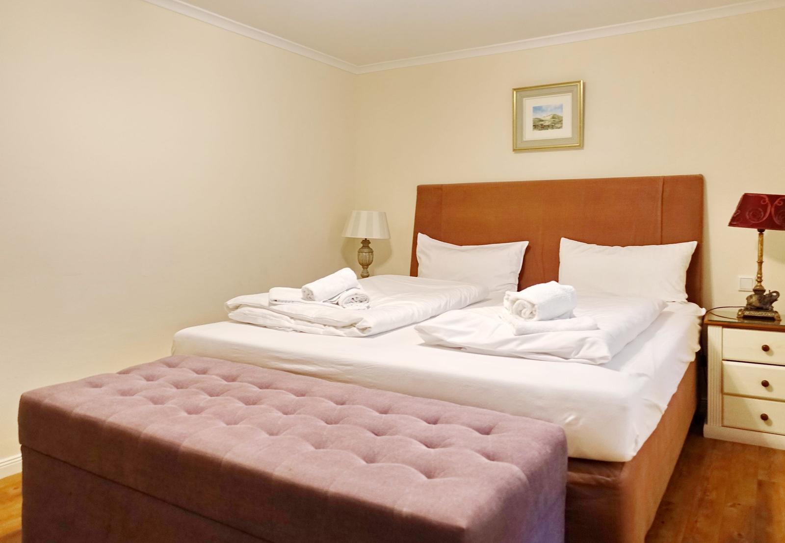 Bedroom with double bed, pink bench, and nightstands with lamps.