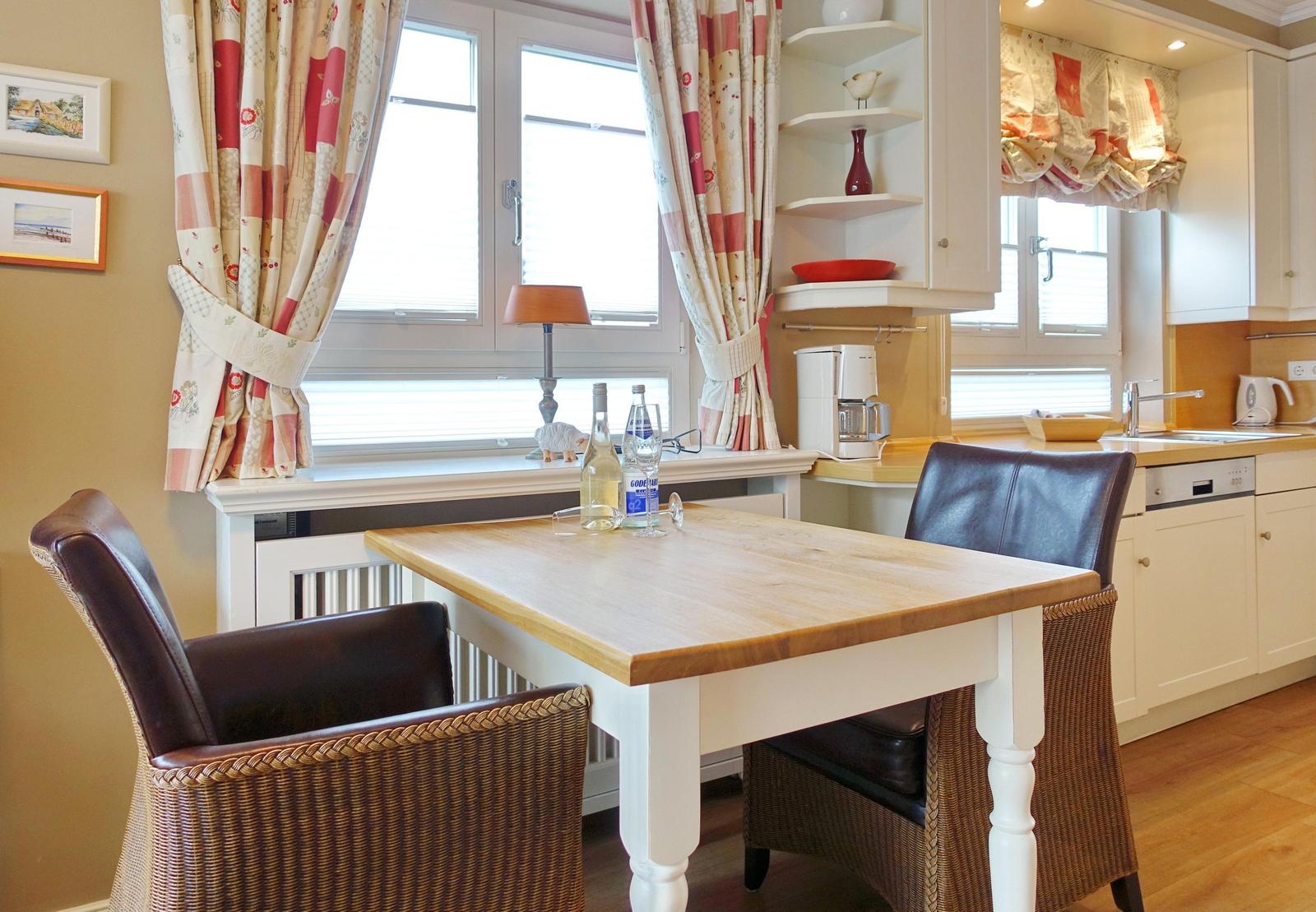 Dining room with table, chairs, and kitchen area. Windows with curtains and kitchen cabinets.