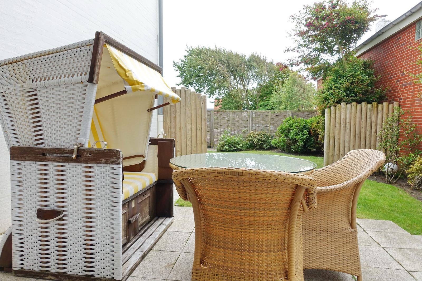Terrace with rattan furniture and beach chair. Background: wooden fence and greenery.