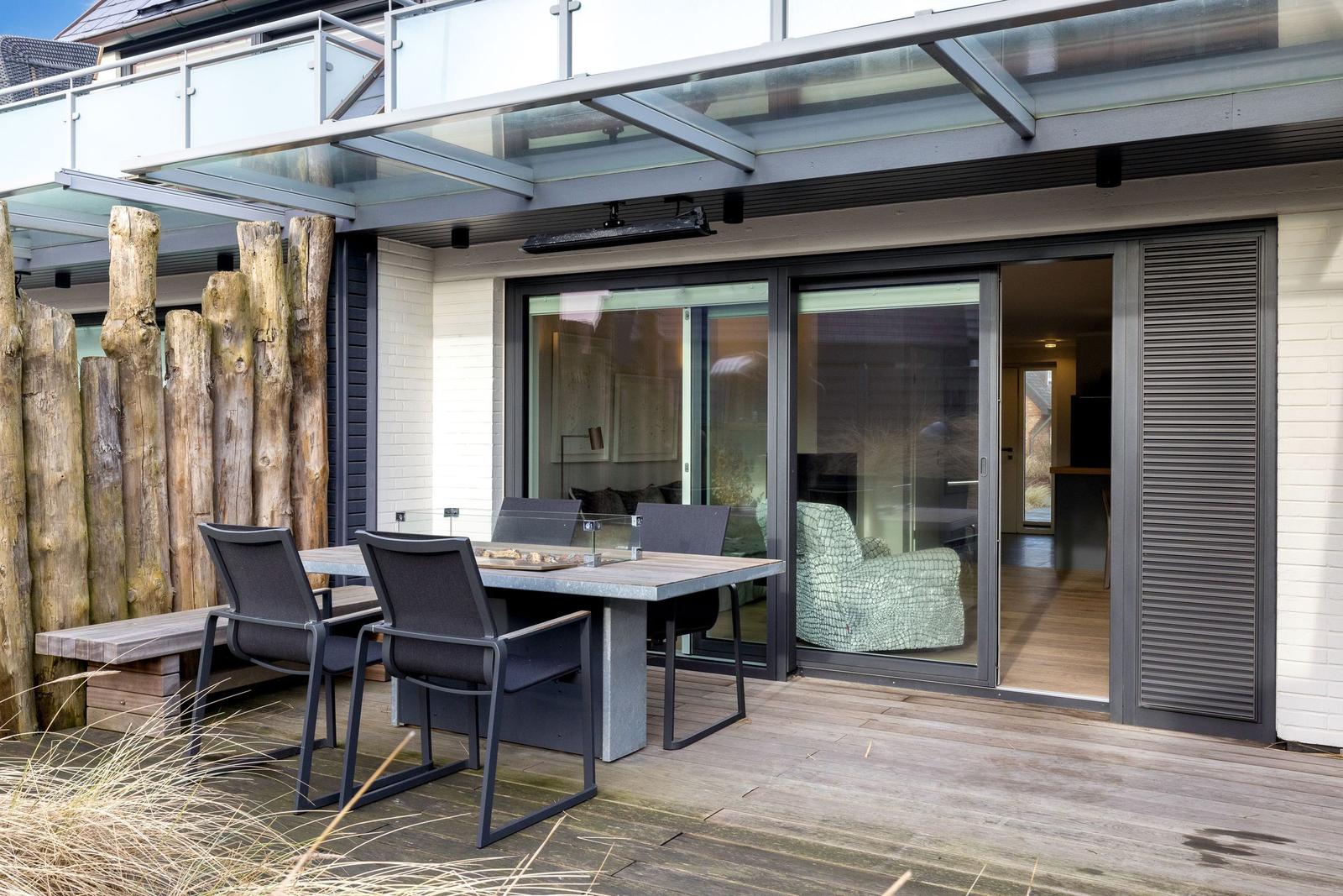 Deck with table, chairs, and wood railing. Glass door opens into the house.