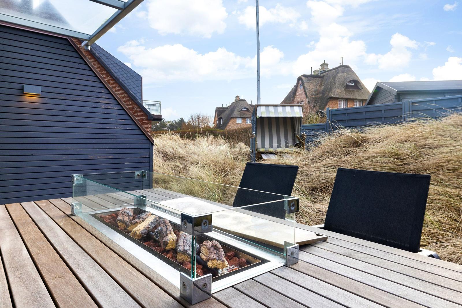 Terrace with fire pit, two chairs, and view of roofs and grass.
